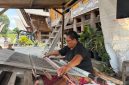 Suasana Desa Tenganan Pegringsingan yang khas dengan tata letak rumah tradisionalnya, mencerminkan kehidupan masyarakat Bali Aga yang teguh menjaga warisan leluhur mereka. Para perempuan Bali Aga tampak tengah menenun kain gringsing, sebuah warisan budaya tak ternilai yang membutuhkan kesabaran dan keahlian tinggi.